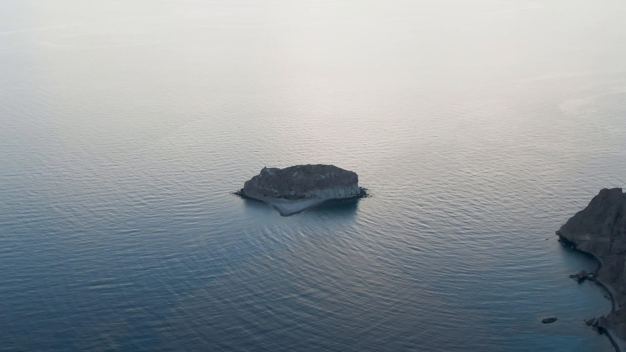 The small rock formation remains over open water while a larger rocky shoreline edge enters from the right at Danzante Bay near Loreto, with no visible people.
