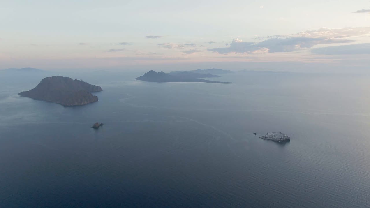 Aerial frame from Danzante Bay Loreto showing the left island slightly nearer in the composition, a small boat below it, a white vessel to the right, distant islands, and no visible people.
