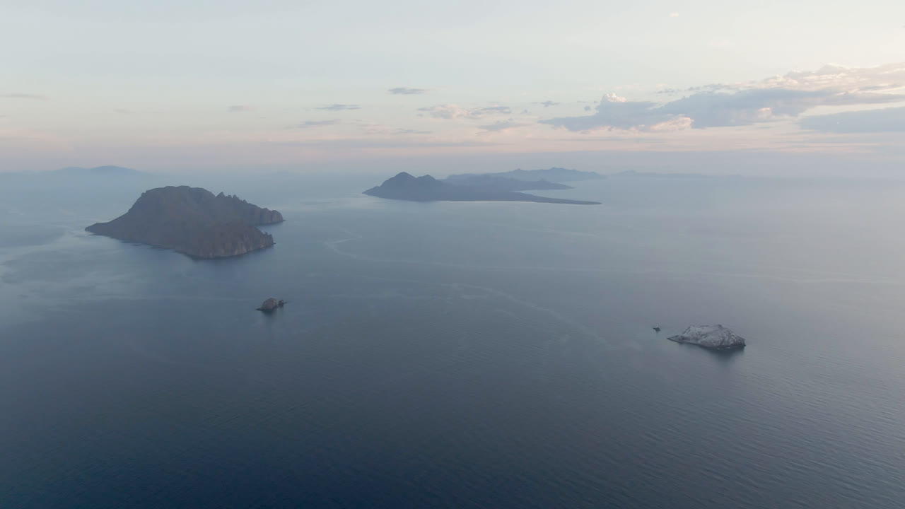 Calm sea with island silhouettes, scattered boats, and soft cloud light.