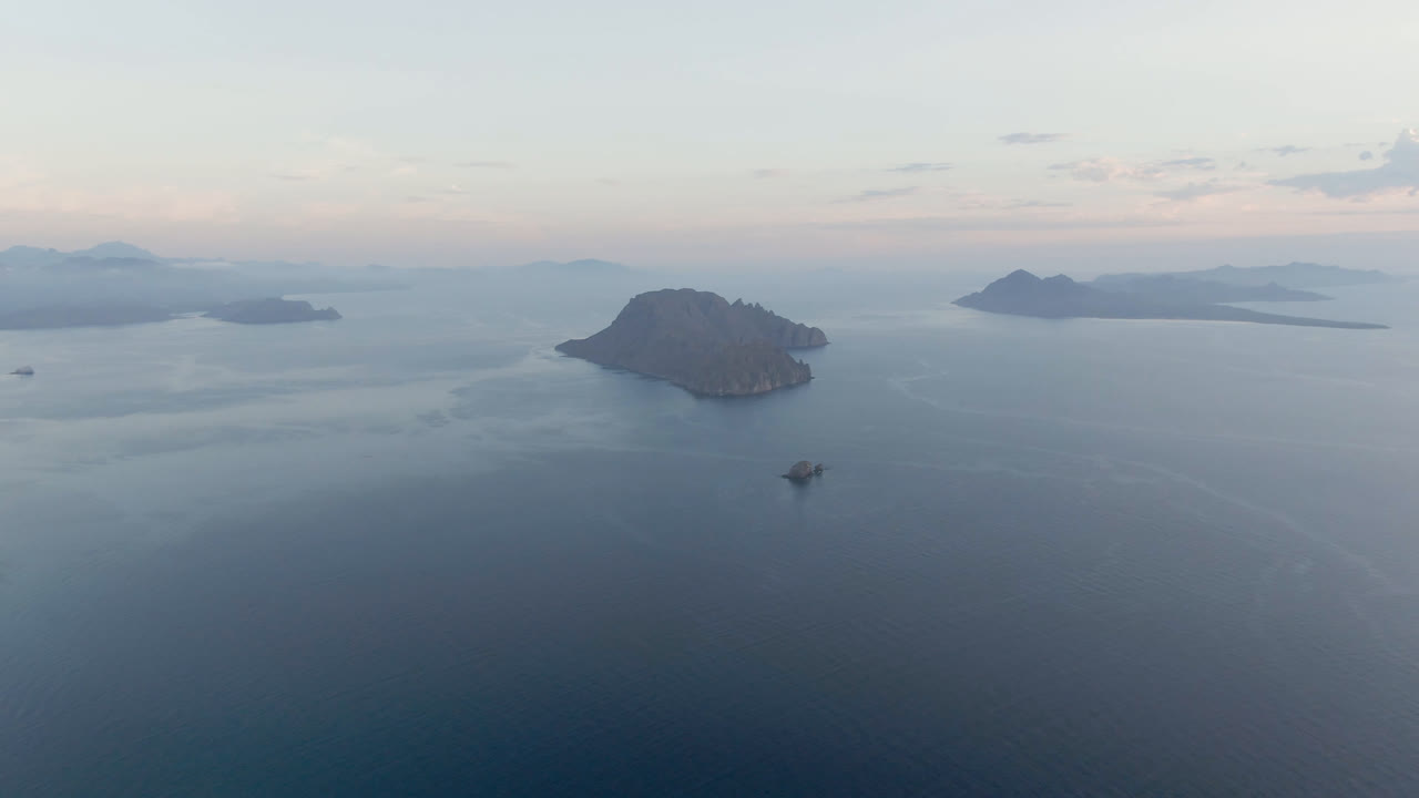 Wide aerial frame over Danzante Bay in Loreto, Baja California Sur, with a small boat below center, broad calm water, distant island silhouettes, pale sky, and no visible people.
