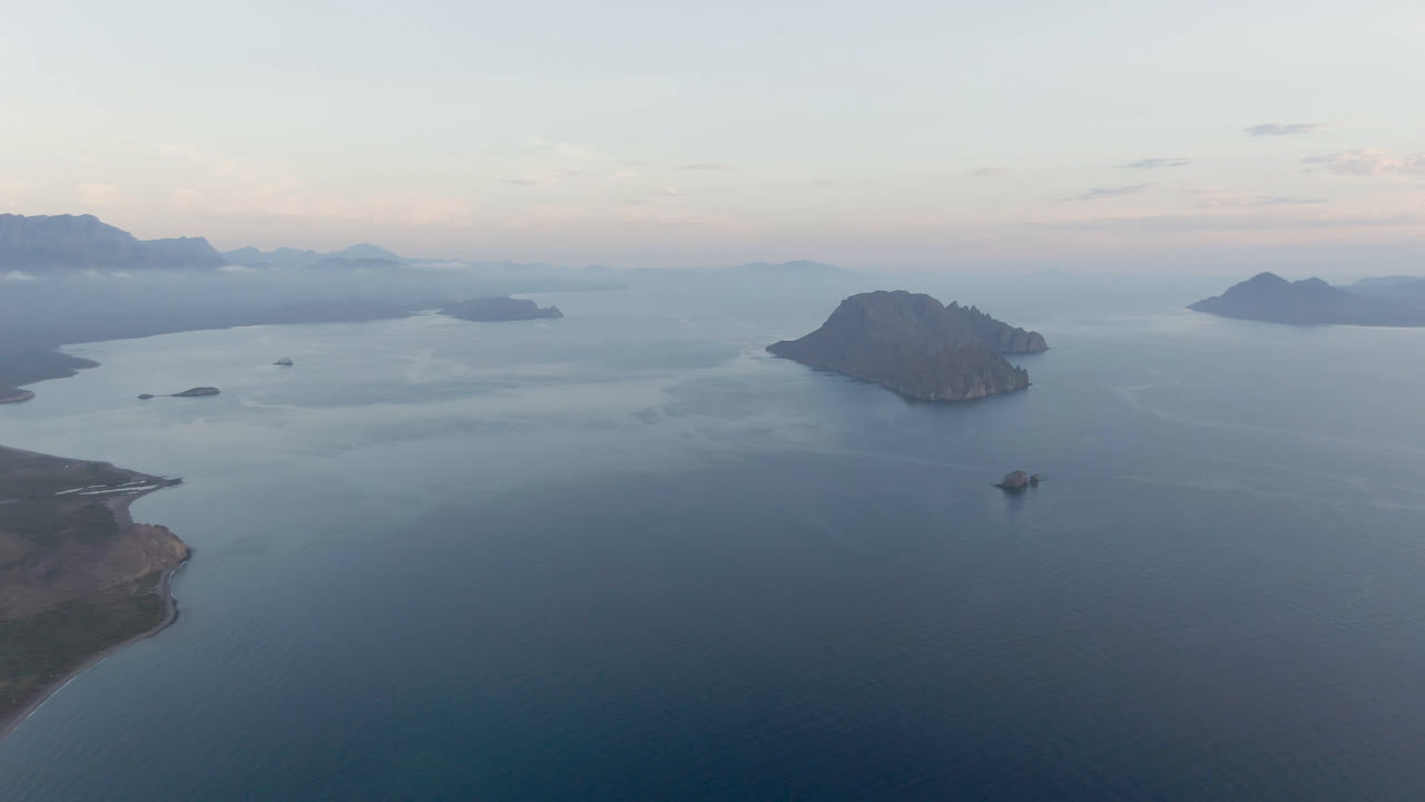 Wide aerial view of blue water, islands, shoreline, and pale sky.