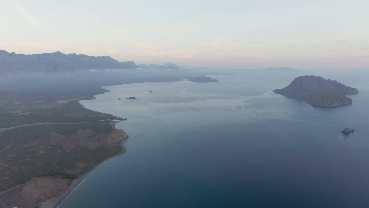 Drone-like bay view with shoreline, island, open water, and hazy mountains