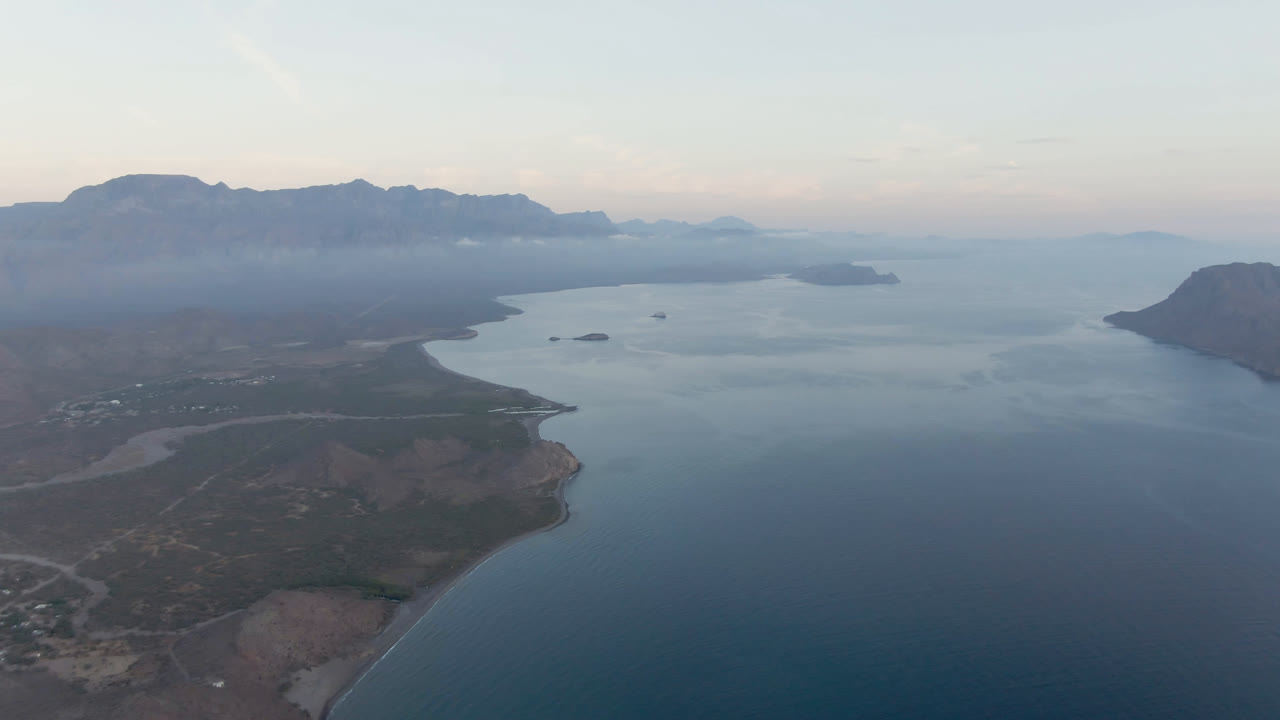 Wide bay aerial with calm water, shoreline, offshore landforms, and mountains