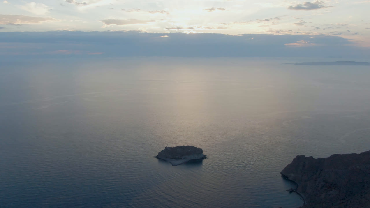 Small offshore rock below a bright cloud reflection