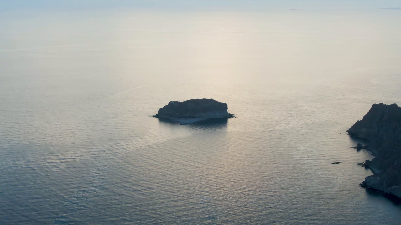 Opening frame of Danzante Bay Loreto, Baja California Sur, with a small rocky island left of center, calm reflective water, a right-edge headland, and no visible people.