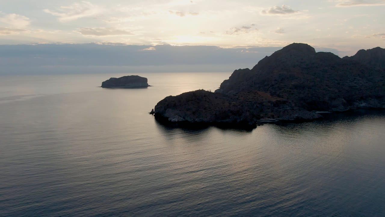 Opening aerial view of Danzante Bay near Loreto, Baja California Sur, with dark rocky islands, calm water, a small island on the left horizon, and no visible people.
