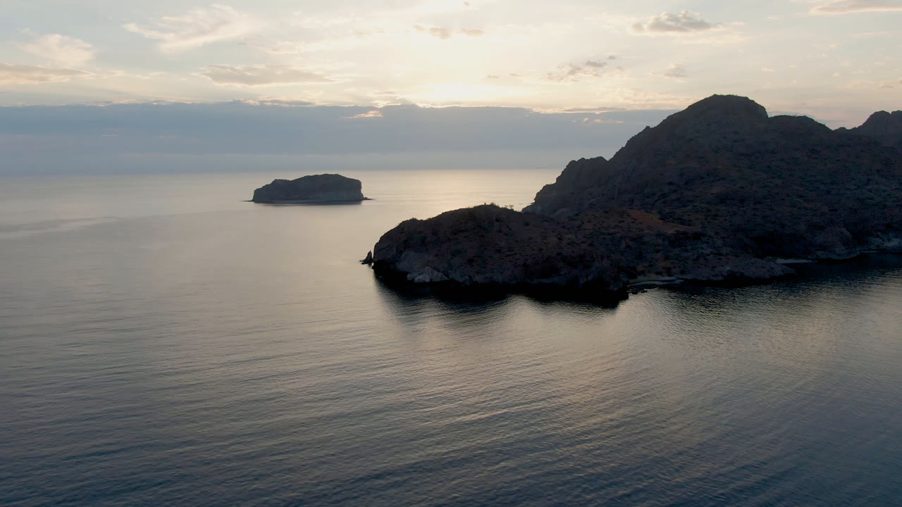 Wide coastal aerial with rocky island silhouettes and still water.