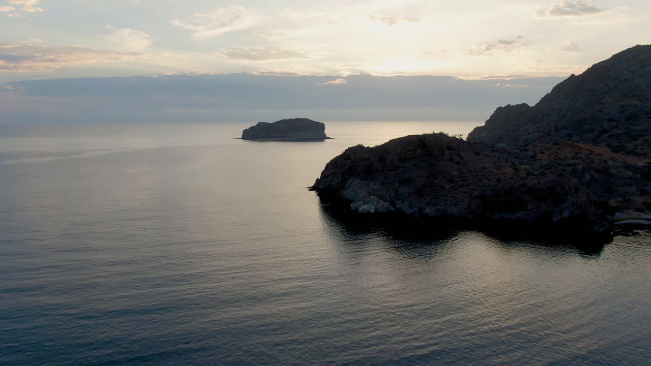 Rocky coastline and offshore island over calm water at dusk.