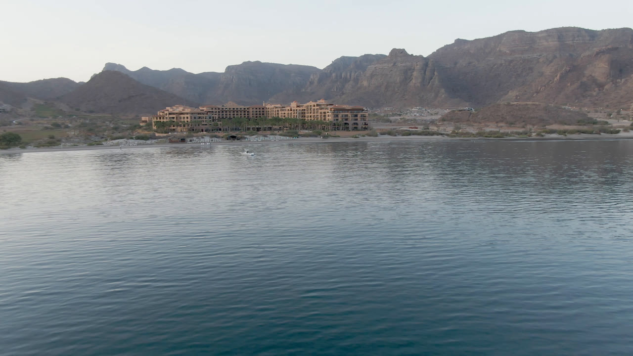 Wide coastal view of calm water, a resort, and mountains