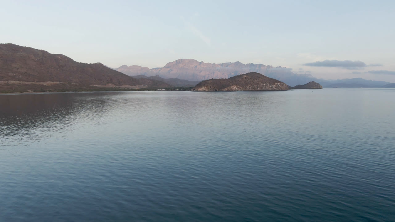 Calm bay water with islands, mountains, and pale sky