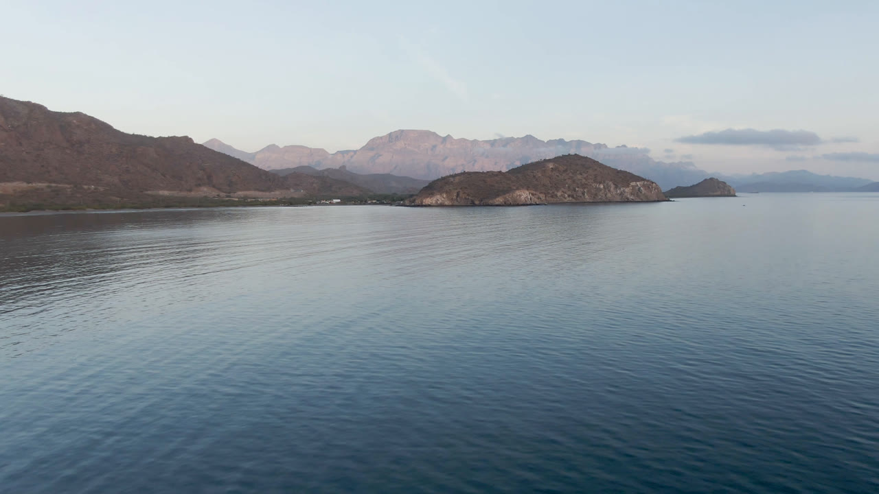 Wide bay water with rocky islands, distant mountains, and pale sky.