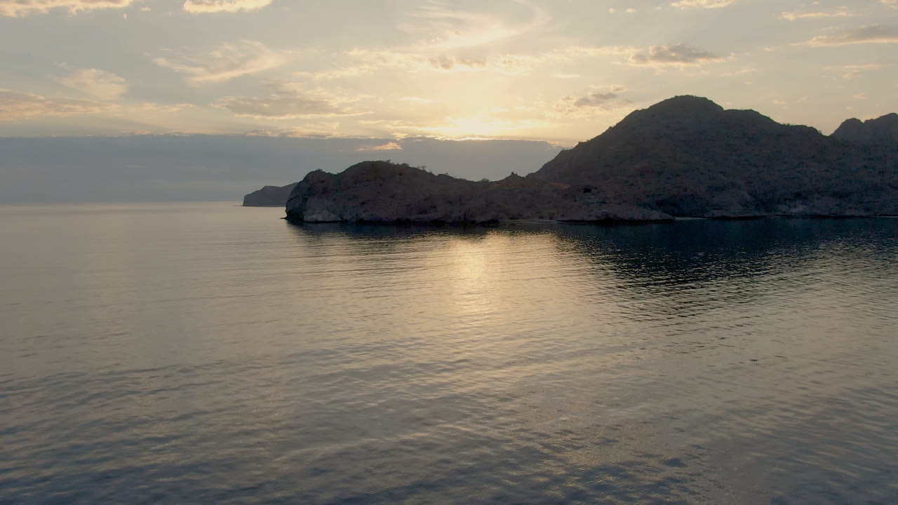 Wide view of calm water and a rocky Danzante Bay shoreline under warm cloud-filtered light, with no visible people.