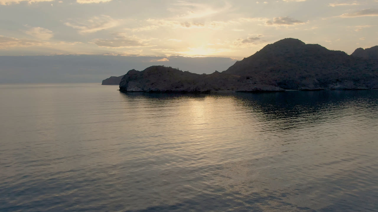 Wide seascape with a rocky island silhouette and soft cloud cover.