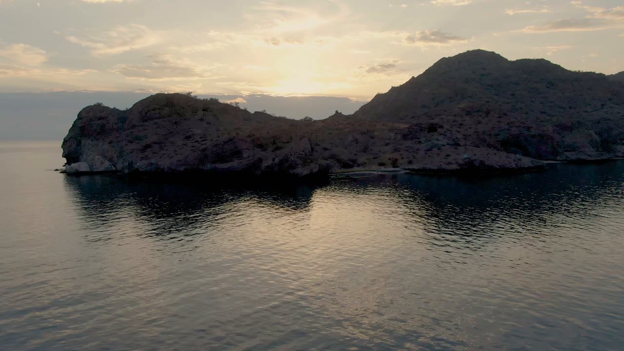Rocky bay and mountain silhouette over calm water at sunset