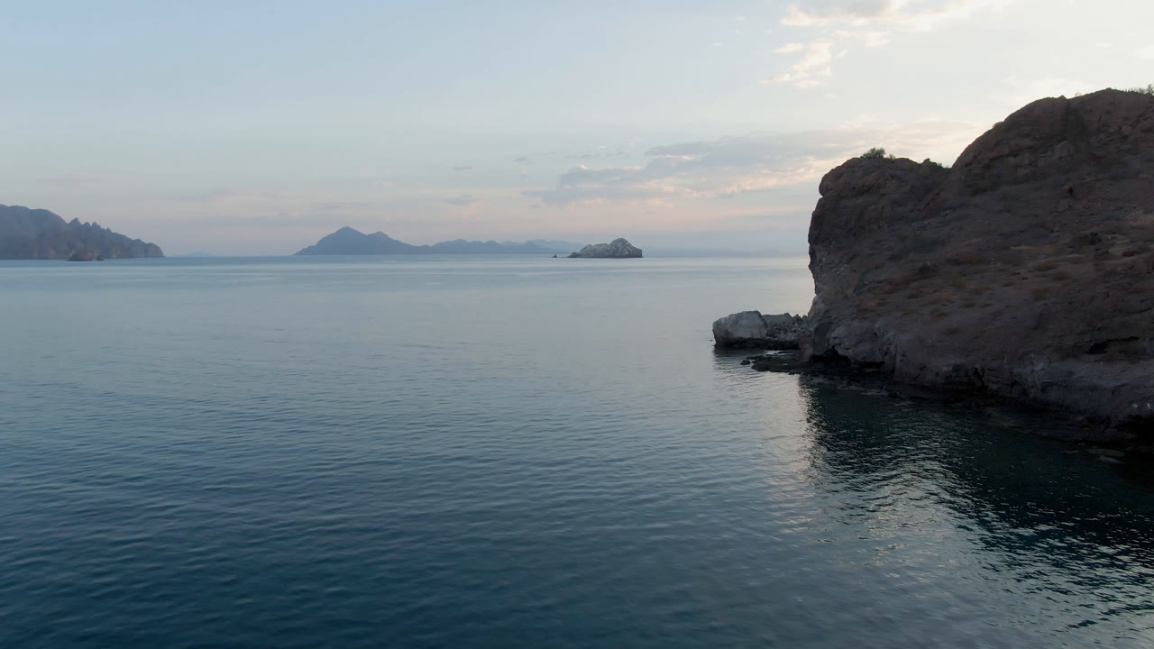 Rocky shoreline beside calm blue water with distant islands on the horizon.
