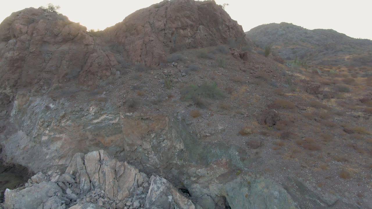 A large reddish rock outcrop dominates the Danzante Bay Loreto hillside, with gray stone layers, scattered brush, and no visible people.
