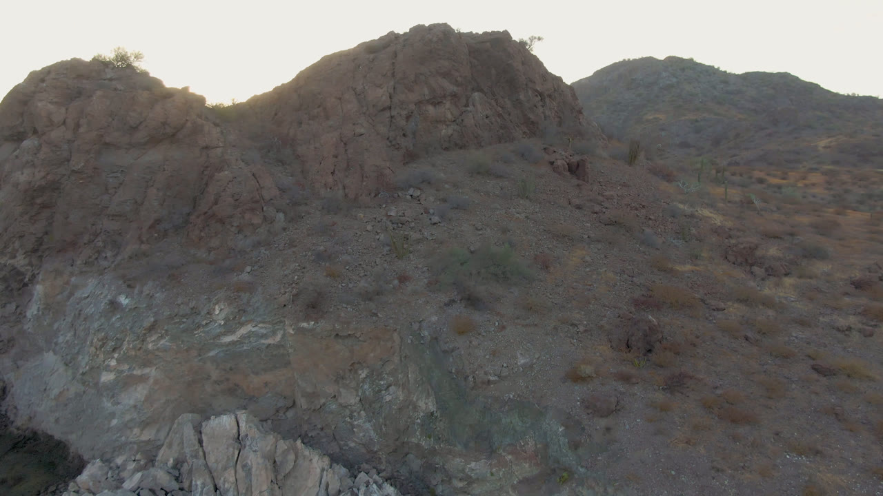 Backlit Danzante Bay Loreto terrain shows a rounded rock mass, scrub-covered slope, distant hills, and no visible people.