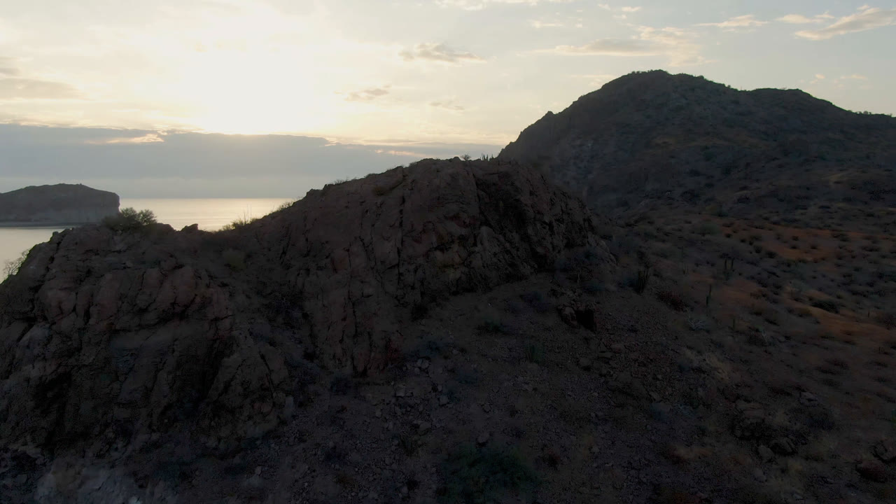 Danzante Bay Loreto rocky hillside and foreground cliff above calm water at dusk, with a pale clouded sky and no visible people.