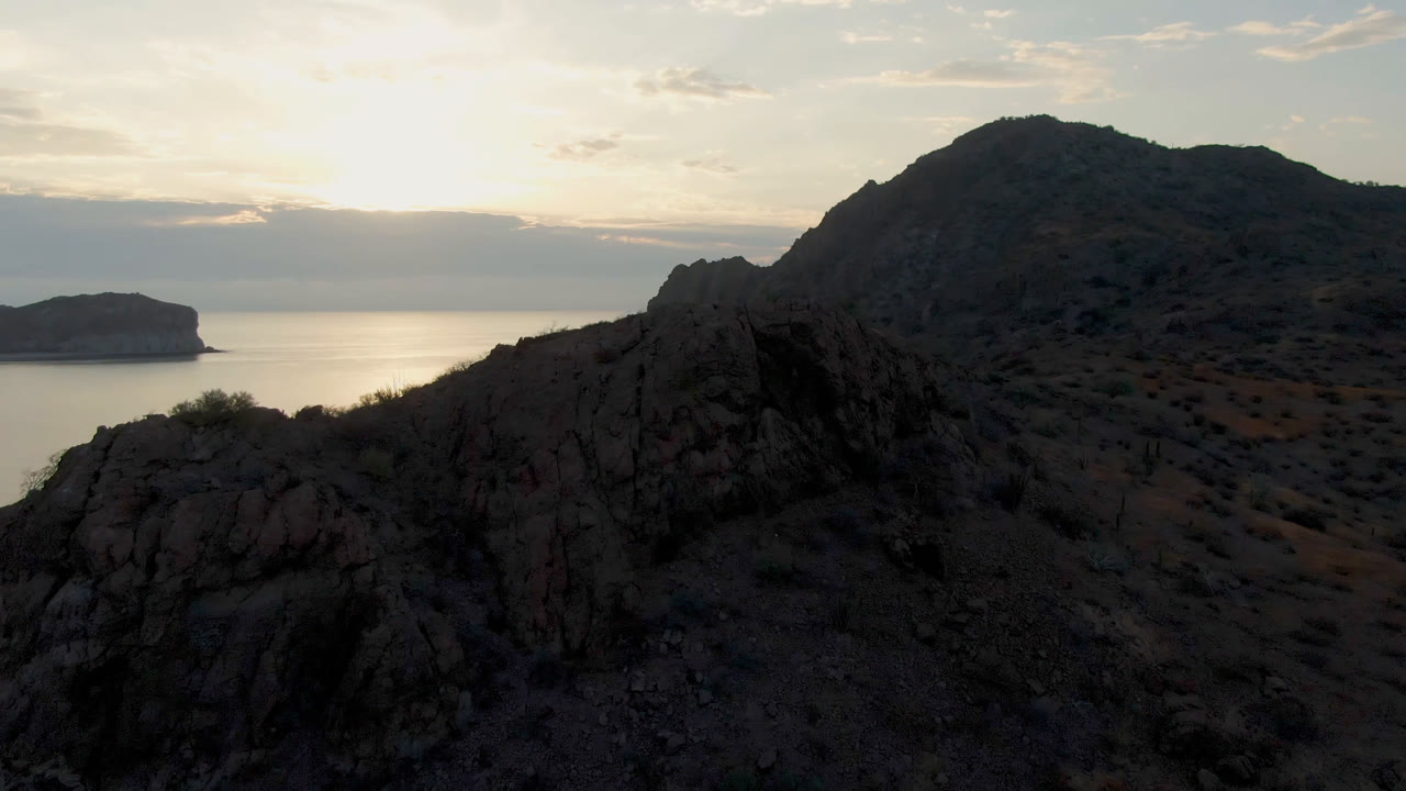 Danzante Bay Loreto cliff ridge fills the foreground while a small offshore landform sits beyond reflective water under dusk clouds, with no visible people.