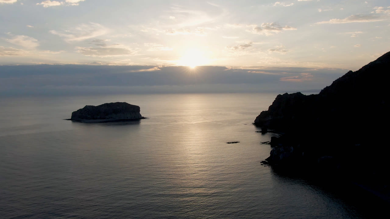 Wide coastal water view with island rock and sunset reflection
