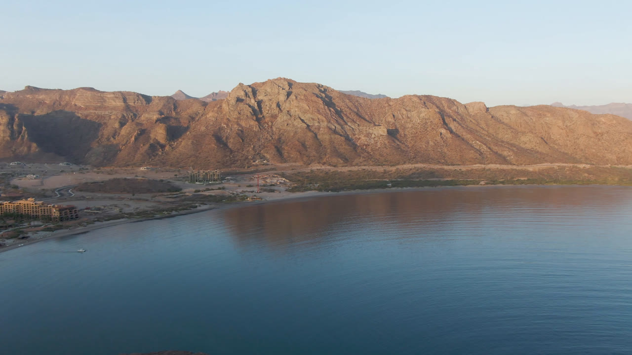 Opening frame of Danzante Bay Loreto with blue water in the foreground, a shoreline at left, rugged brown mountains in the background, clear sky, and no visible people.