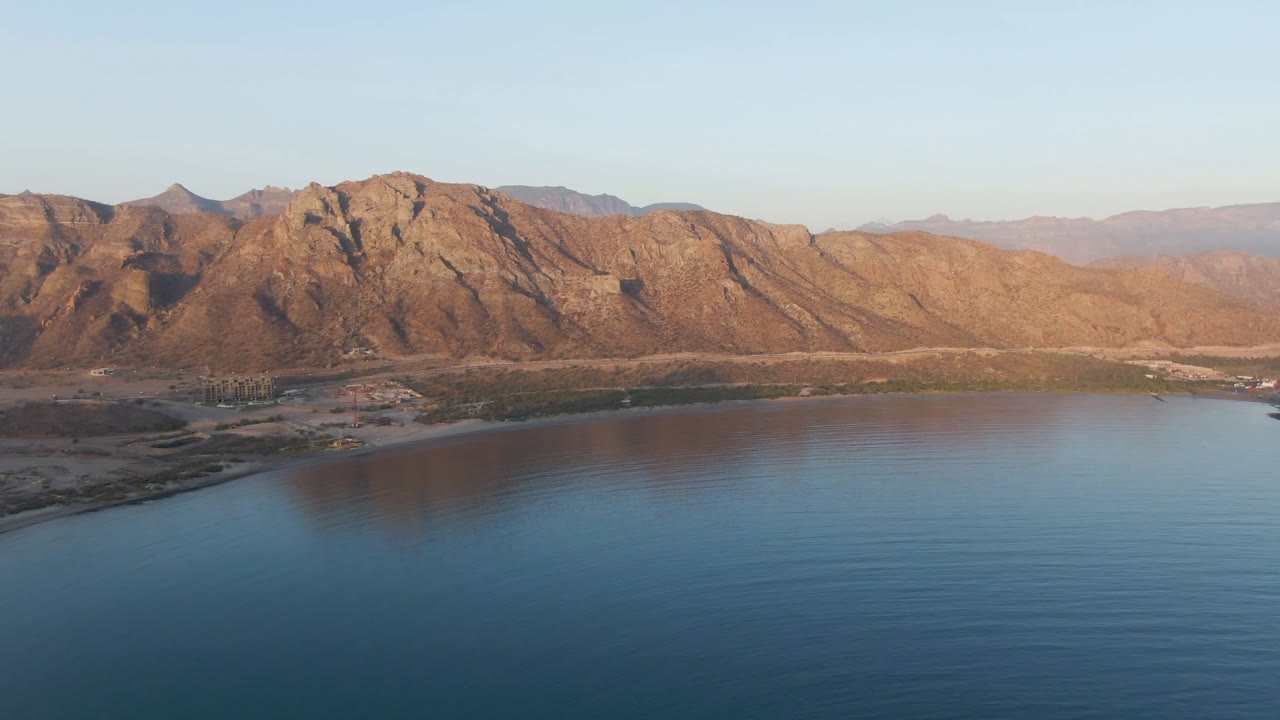 Wide aerial coastline with calm water and mountain backdrop.