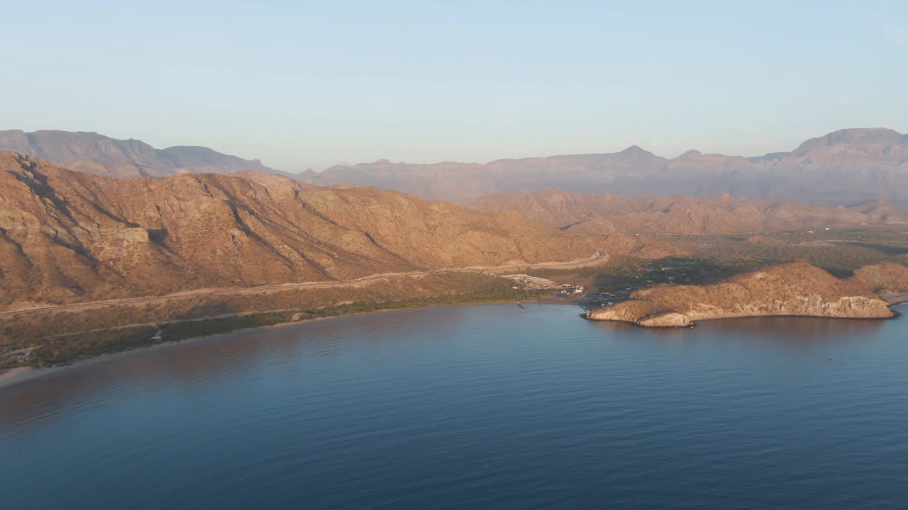 Blue bay water below a small island and sunlit mountain range