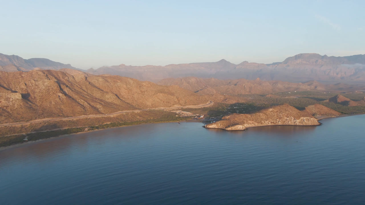 Aerial view across calm water toward a rocky island and mountain coastline
