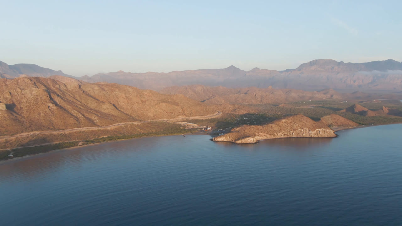 Wide bay landscape with dark blue water, rocky shore, and sunlit ridges