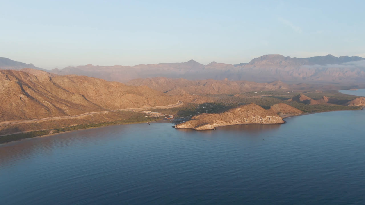 Wide aerial view of blue water, rocky shoreline, islands, and distant mountains.