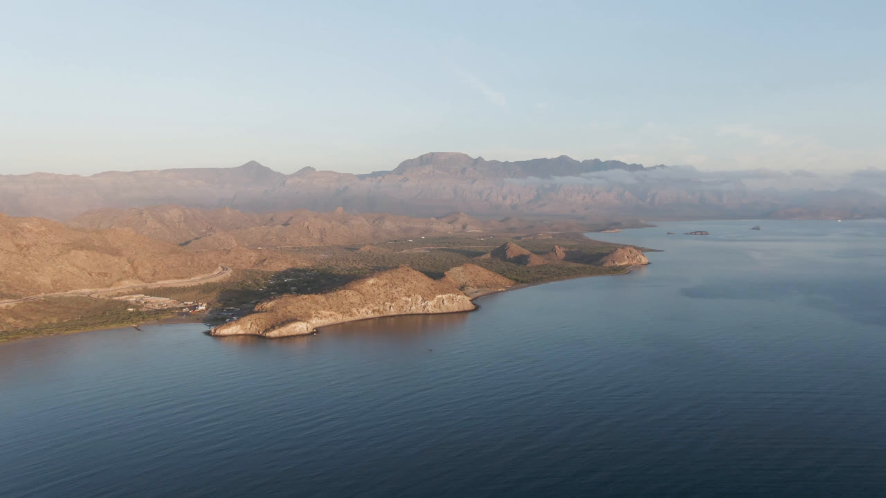 Aerial coastal landscape with ocean, headland, and mountain horizon.