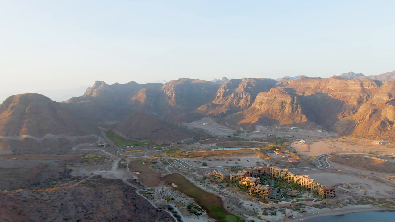 Aerial landscape with mountains, desert roads, buildings, and water in the foreground.