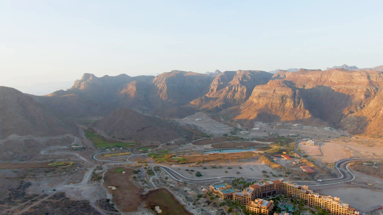 Aerial view at Danzante Bay Loreto with the resort lower in frame, graded desert lots and roads across the valley, and rocky mountains beyond with no visible people.