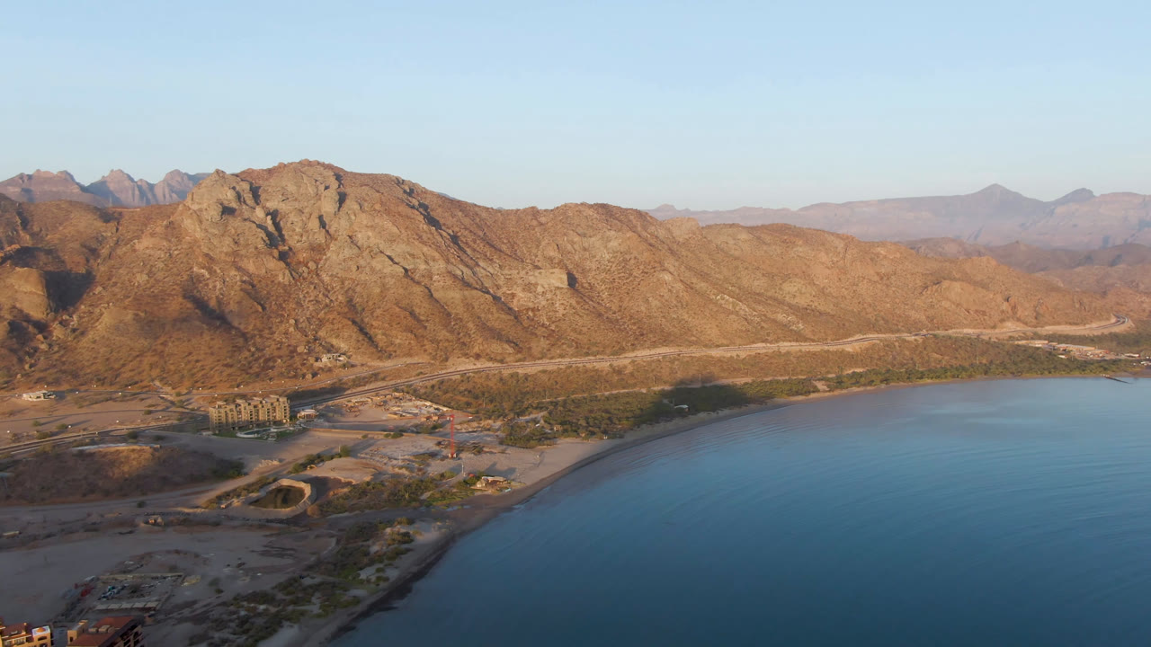 Rocky coastal mountains rise above blue water and a narrow shore.