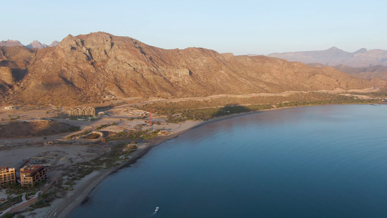Wide aerial of Danzante Bay coastline with mountains and small boat on the water.