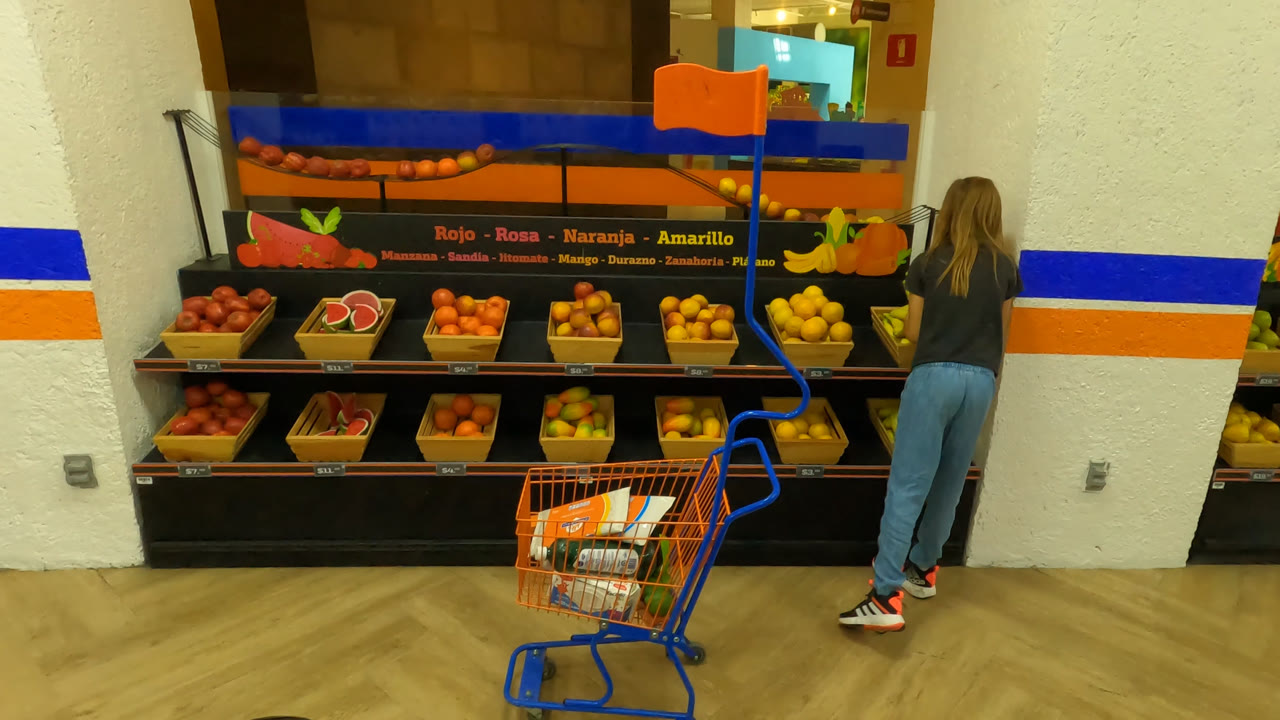 A child in Mexico City reaches toward bananas on the right side of a fruit stand as the shopping cart remains in front of the display.