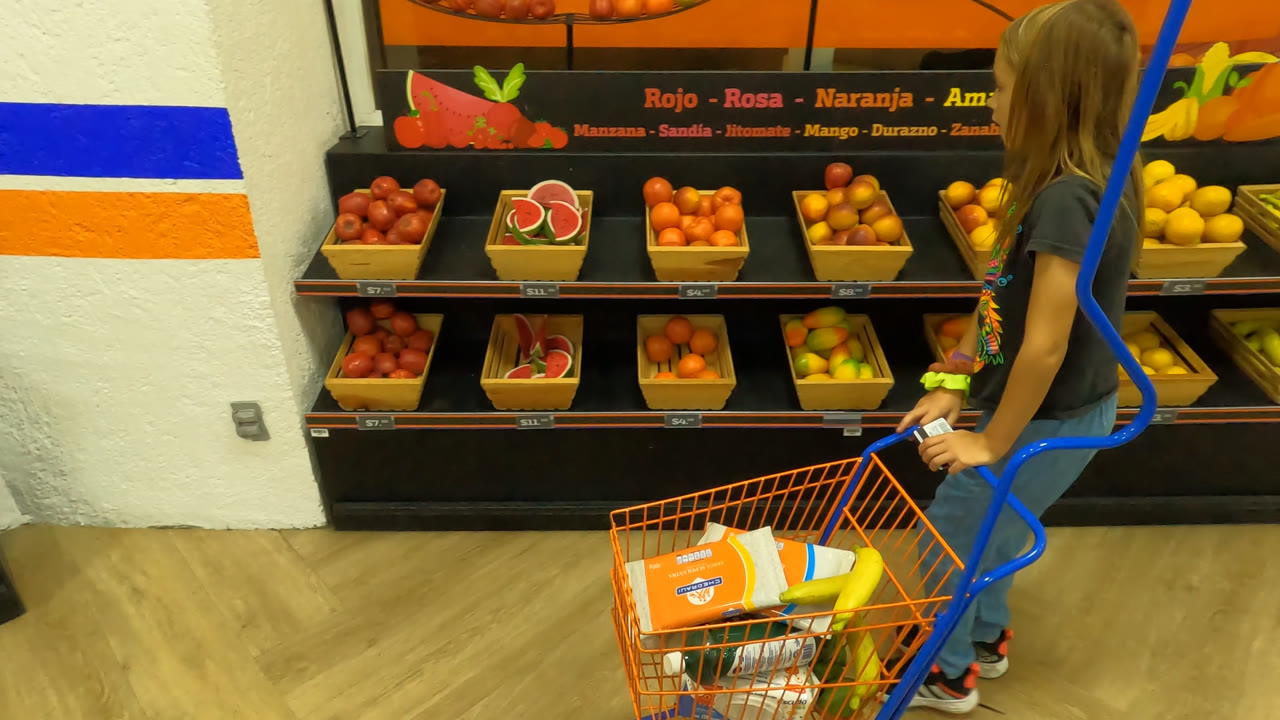 Girl steers a shopping cart toward produce shelves.