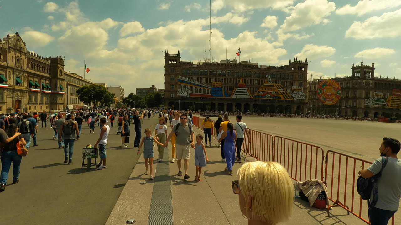 Crowds walking across a large plaza with historic buildings and cloudy sky.