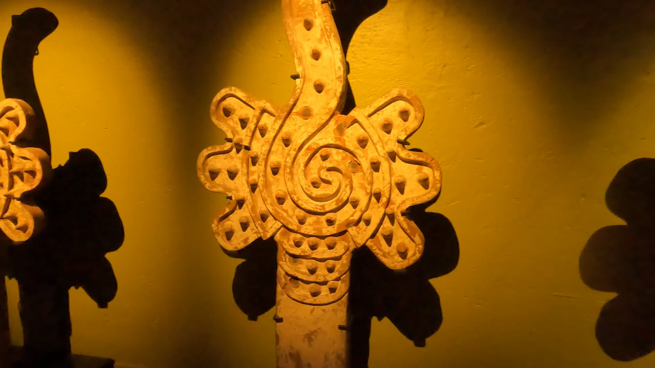 Close view of a spiral-patterned wooden carving on display in Mexico City, with warm light and a dark shadow on the yellow wall.
