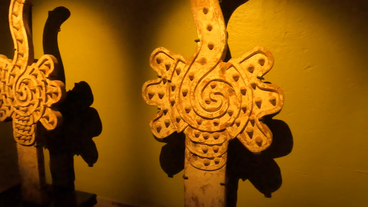 Side angle on two wooden carvings in a Mexico City museum, with the nearer vertical piece partly obscuring the second and no visible people.