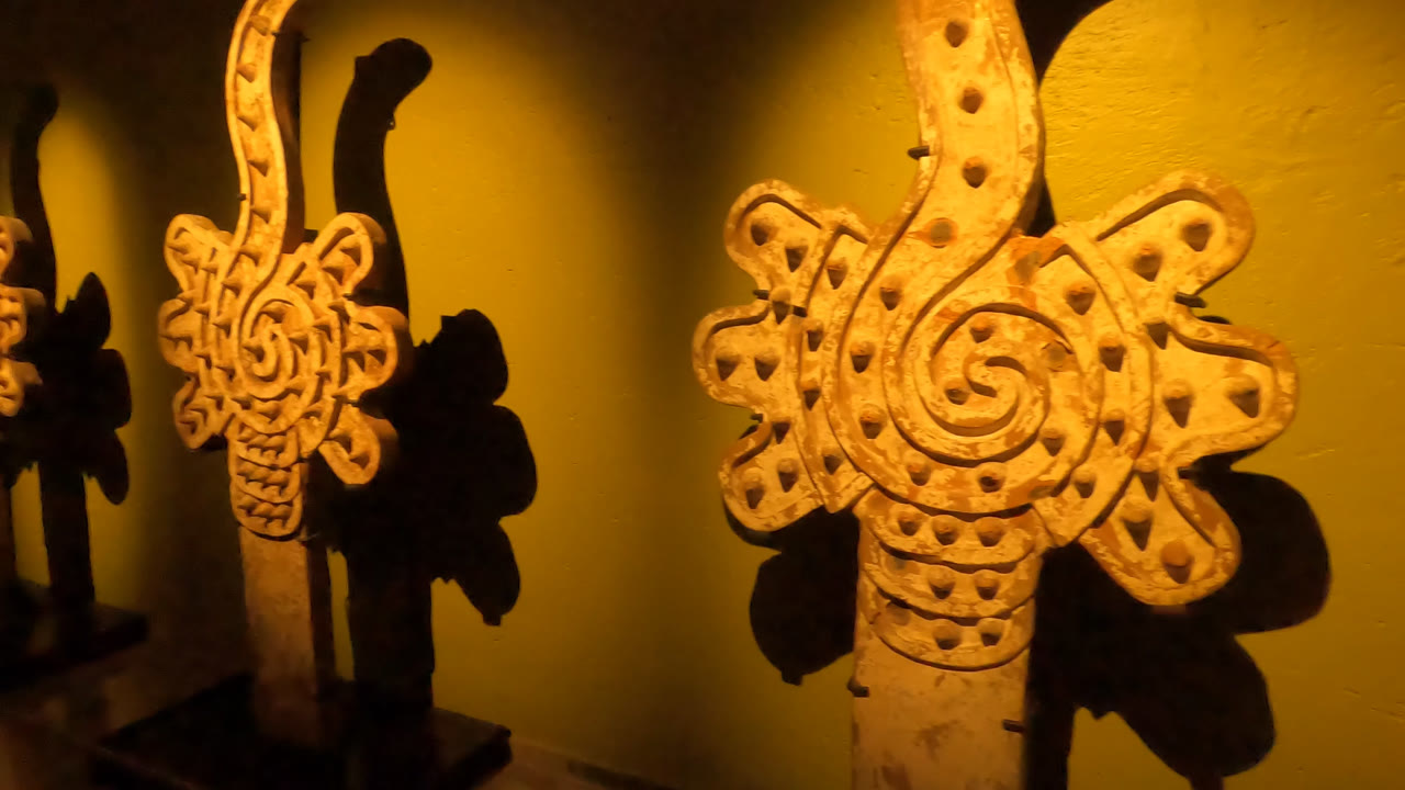 Front-facing detail of the central spiral and dotted carving on a wooden museum artifact in Mexico City, with no visible people.