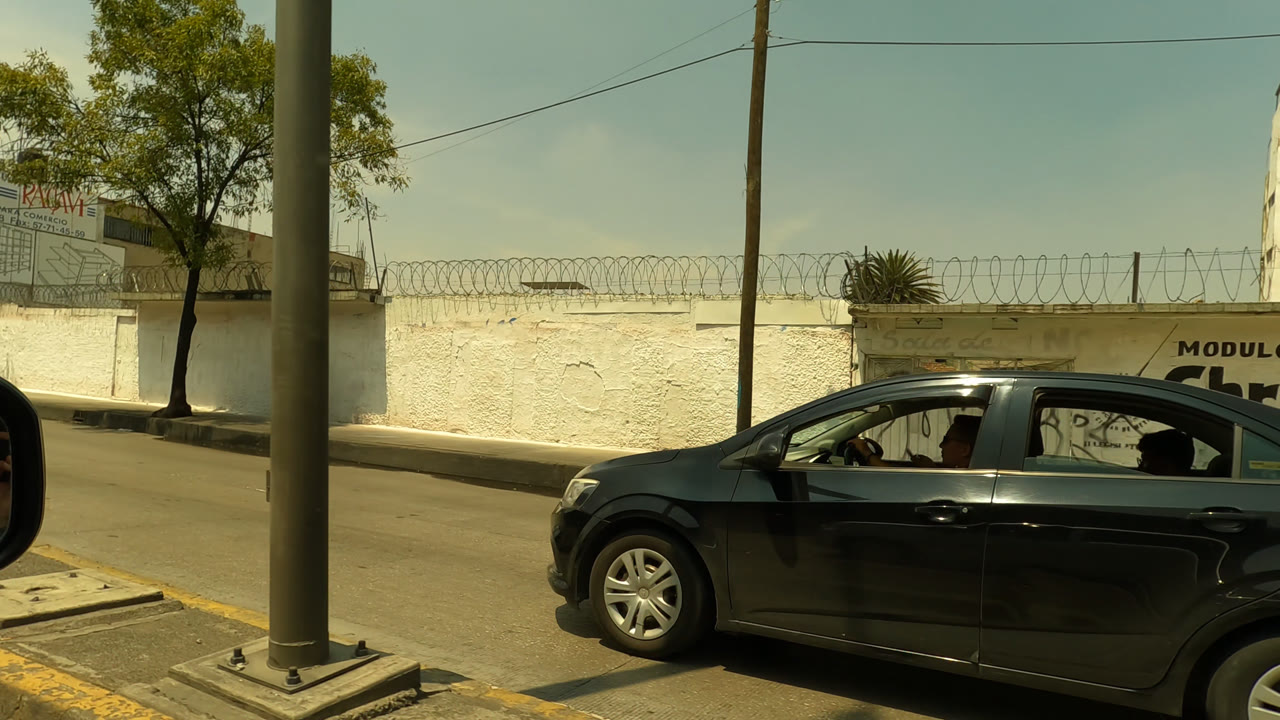 Black sedan beside a white wall and street pole.