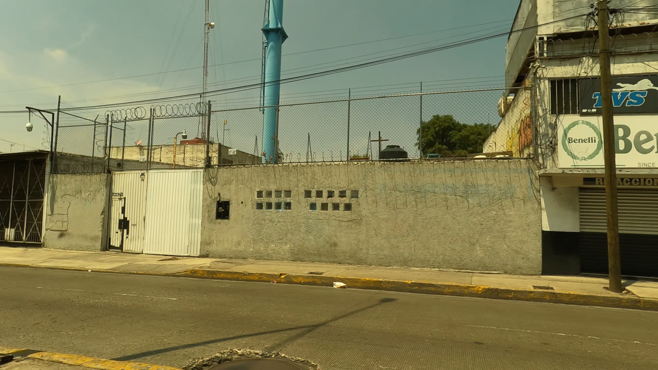 Street-level view in Mexico City showing a walled corner, utility poles, overhead wires, and visible commercial signage above a building, with no visible people.