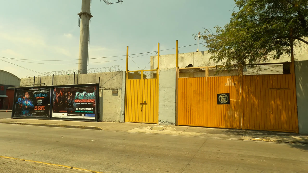 Wide street view with yellow gates, posters, wall, tree, and utility pole.