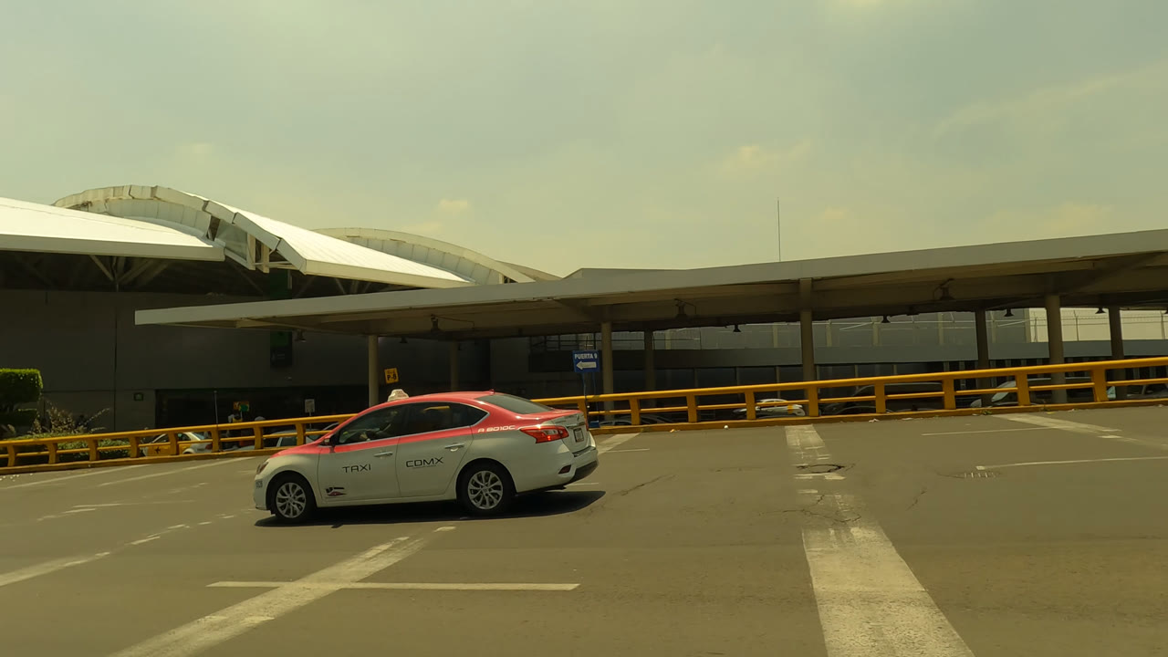 White and red taxi driving past an airport terminal curb lane.