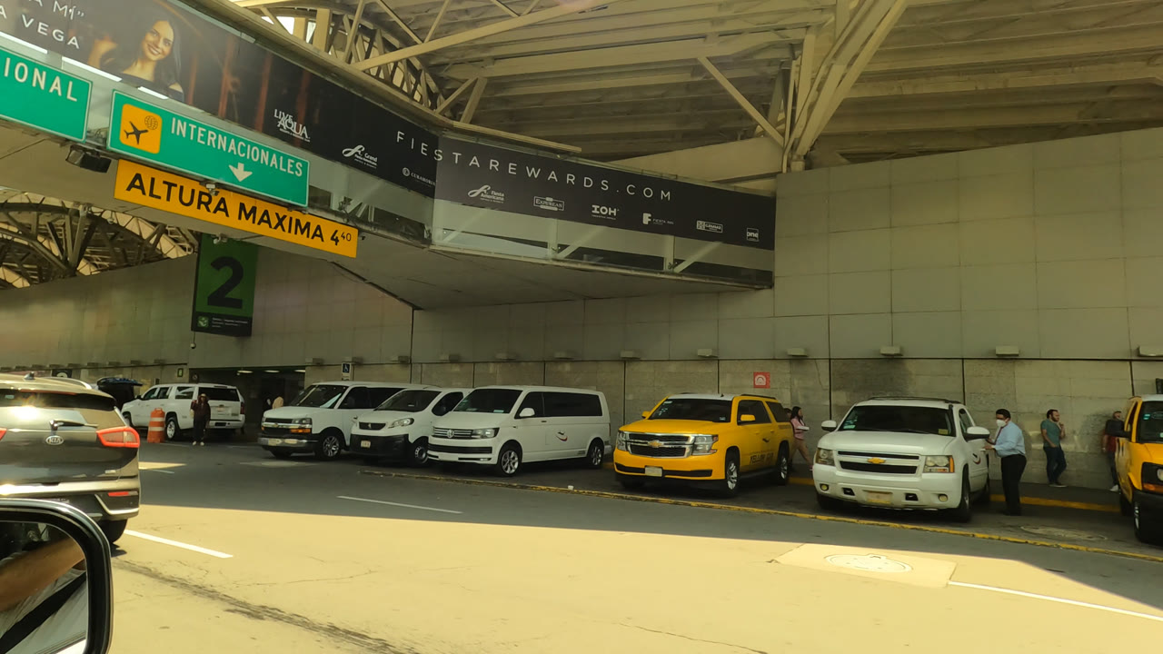 Covered airport curb with taxis, vans, signs, and vehicles waiting.
