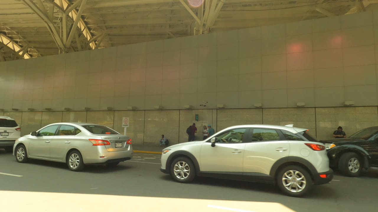 Cars outside a covered airport terminal curb with wall panels and roof trusses.