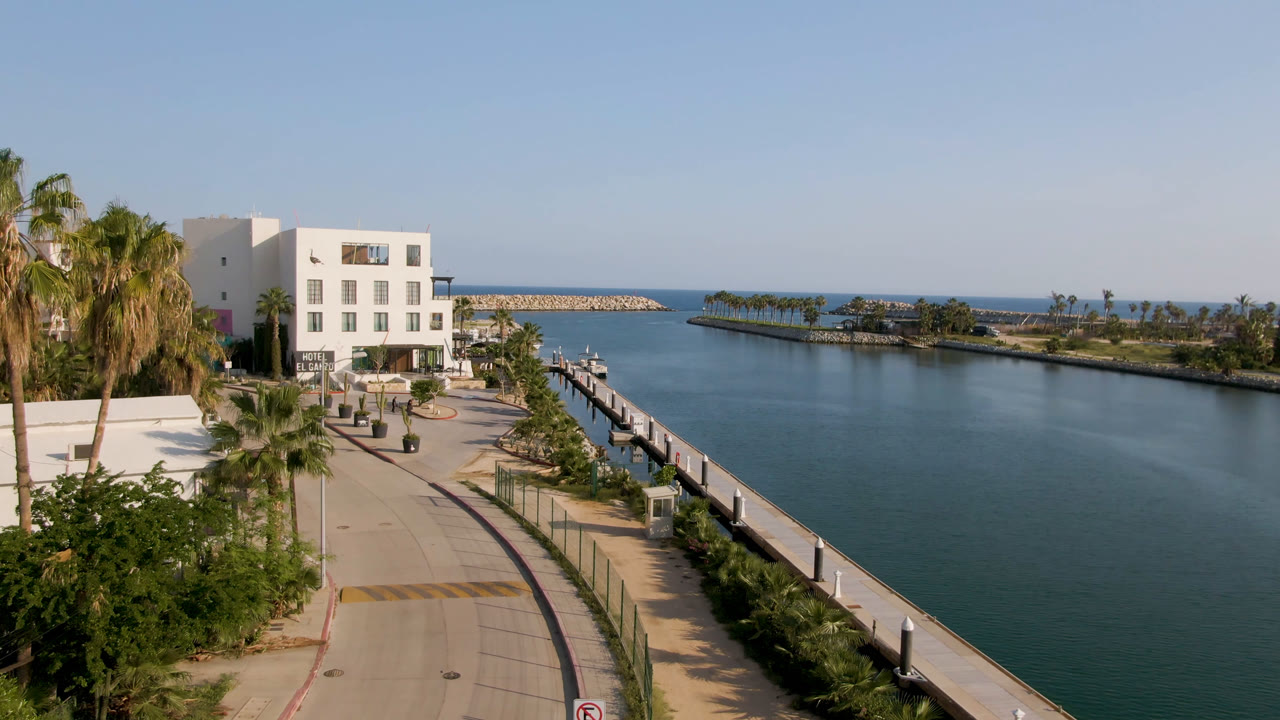Elevated view of a waterfront road, palms, white building, and blue channel