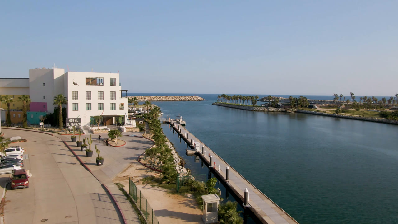 Elevated view of a white waterfront hotel beside a dock and calm water.