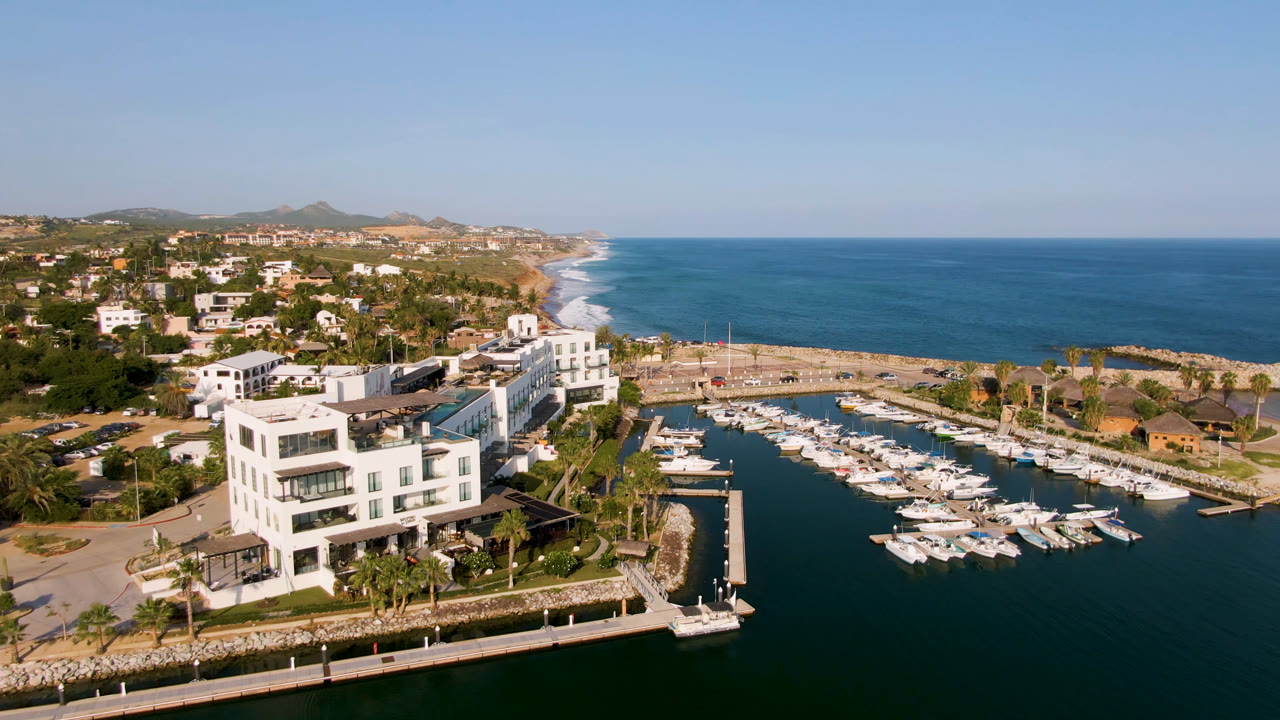Aerial view of a marina with docked boats beside a white waterfront building and ocean beyond.
